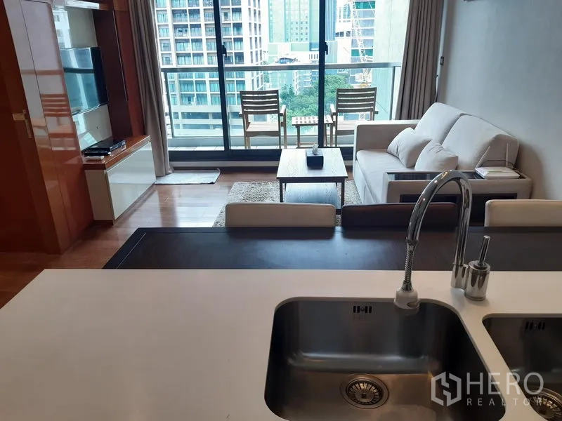 公寓 出租在Khlong Toei, Bangkok - 开放式客厅配沙发与茶几，连通带椅子的阳台，可赏曼谷天际线，视角来自带双水槽的中岛厨房。