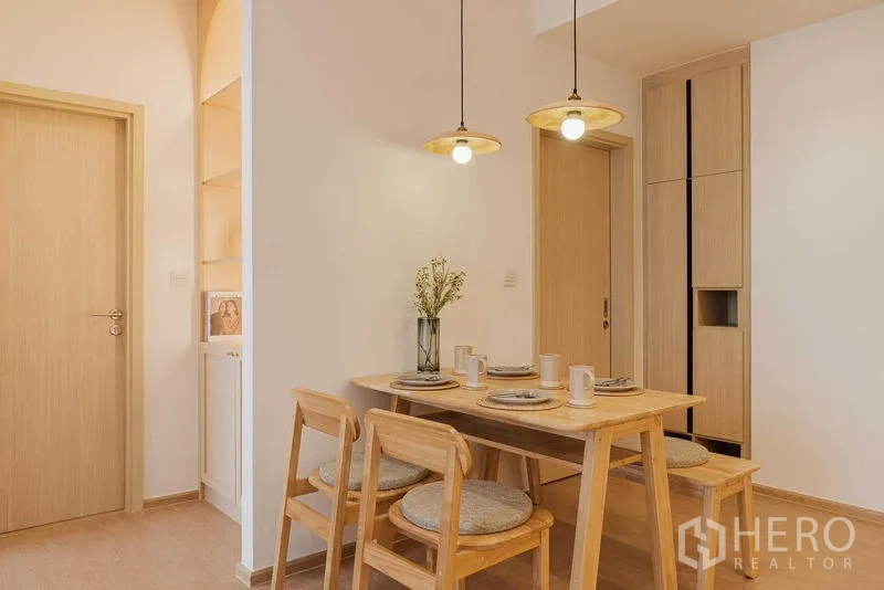 Condominium for rent in Watthana, Bangkok - Compact dining nook with wooden furniture and two hanging lamps.