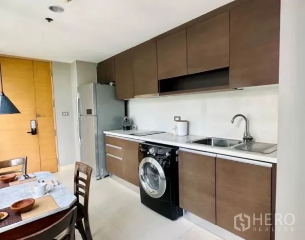 Condominium for rent in Watthana, Bangkok - Modern galley kitchen with wood cabinets, washer, fridge and double sink.