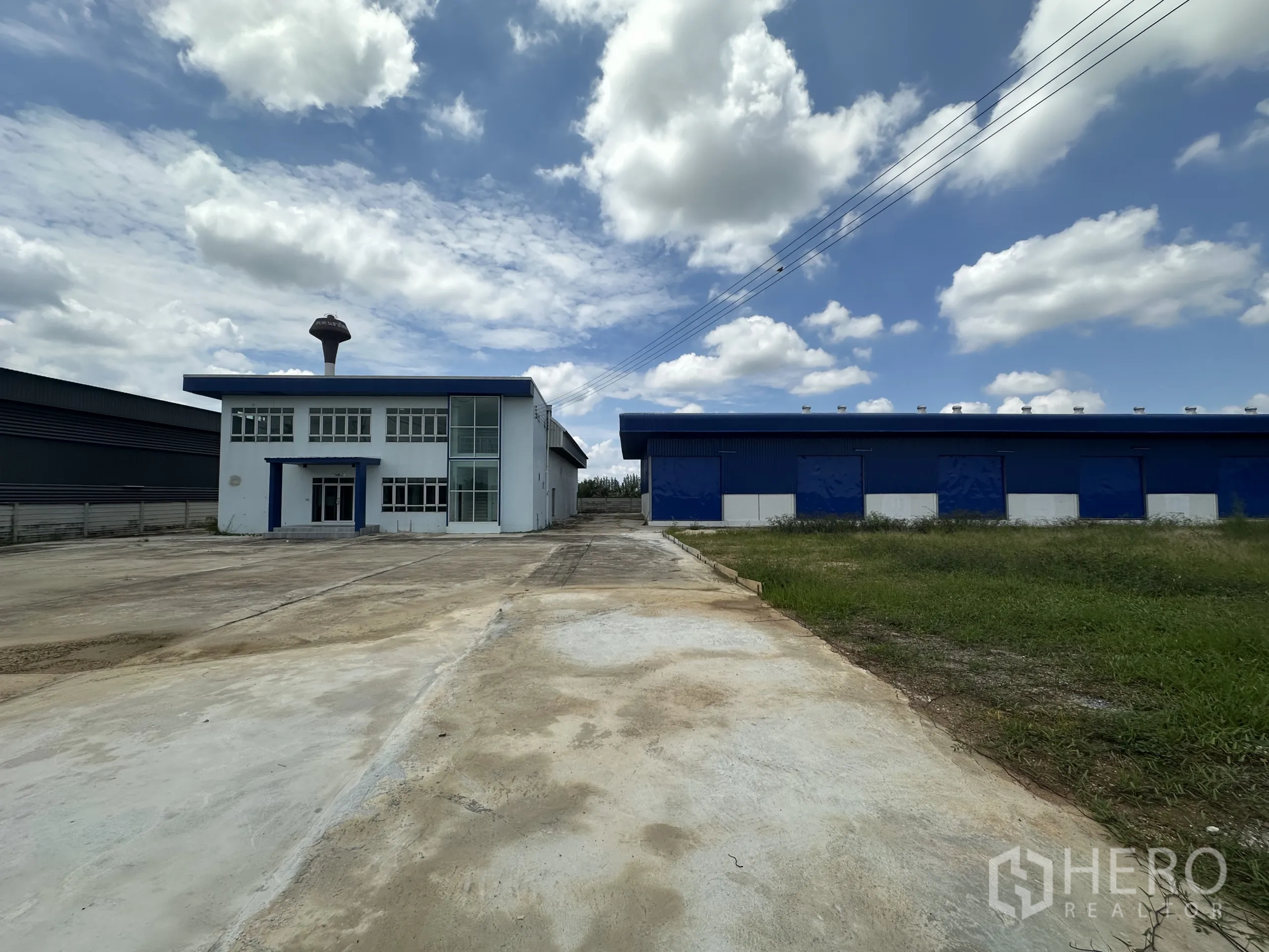 Warehouse for rent in Bang Len, Nakhon Pathom - Panoramic shot of driveway, lawn and warehouse complex under blue sky.
