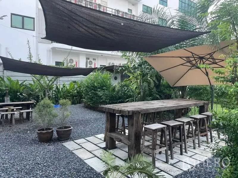 พื้นที่ขายปลีก ให้เช่าในSuan Luang, Bangkok - พื้นที่นั่งเล่นกลางแจ้งมีโต๊ะไม้ยาว ม้านั่ง และร่มขนาดใหญ่ ท่ามกลางสวนร่มรื่นของพื้นที่ค้าปลีก