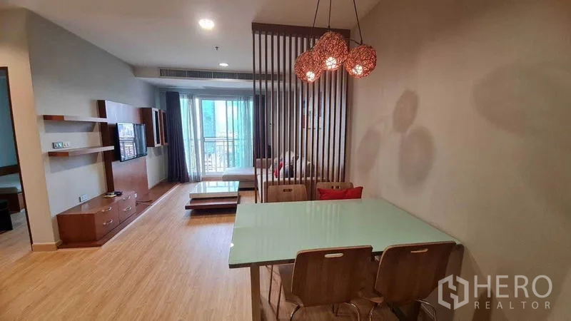 Condominium for rent or sale in Watthana, Bangkok - Open-plan living and dining with glass-top table, pendant lights, wooden slat partition, and balcony beyond.