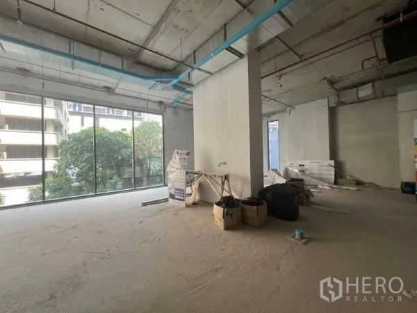 零售空间 出租在Khlong Toei, Bangkok - 未完成装修的店铺内部，中央立柱、蓝色管线与通高落地窗朝向街景。