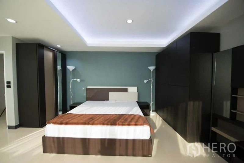 公寓 出租在Khlong Toei, Bangkok - 主卧配大床、深色衣柜、蓝色背景墙与灯槽天花。