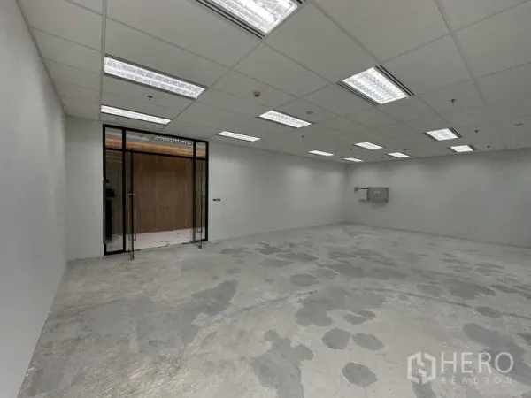 Office Space for rent in Ratchathewi, Bangkok - Interior of empty office showing glass entry doors, bright grid ceiling lights, and raw concrete floor.