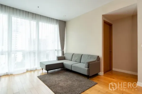 คอนโด ให้เช่าในKhlong Toei, Bangkok - ห้องนั่งเล่นสว่าง โซฟาเข้ามุม ผ้าม่านโปร่ง และหน้าต่างสูงจรดเพดานบนพื้นไม้โทนอุ่น