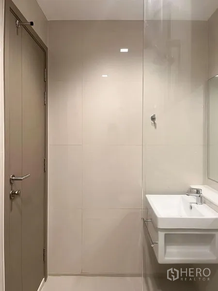 Condominium for sale in Ratchathewi, Bangkok - Dining space by the balcony with city-facing glass door and two wooden chairs.