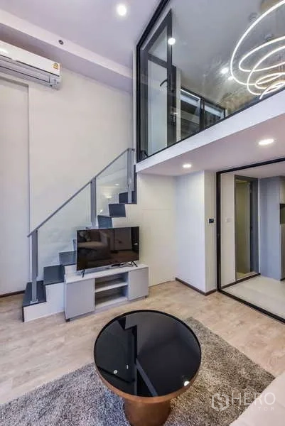 Condominium for rent in Huai Khwang, Bangkok - Staircase with glass railing leading to mezzanine and TV cabinet below.