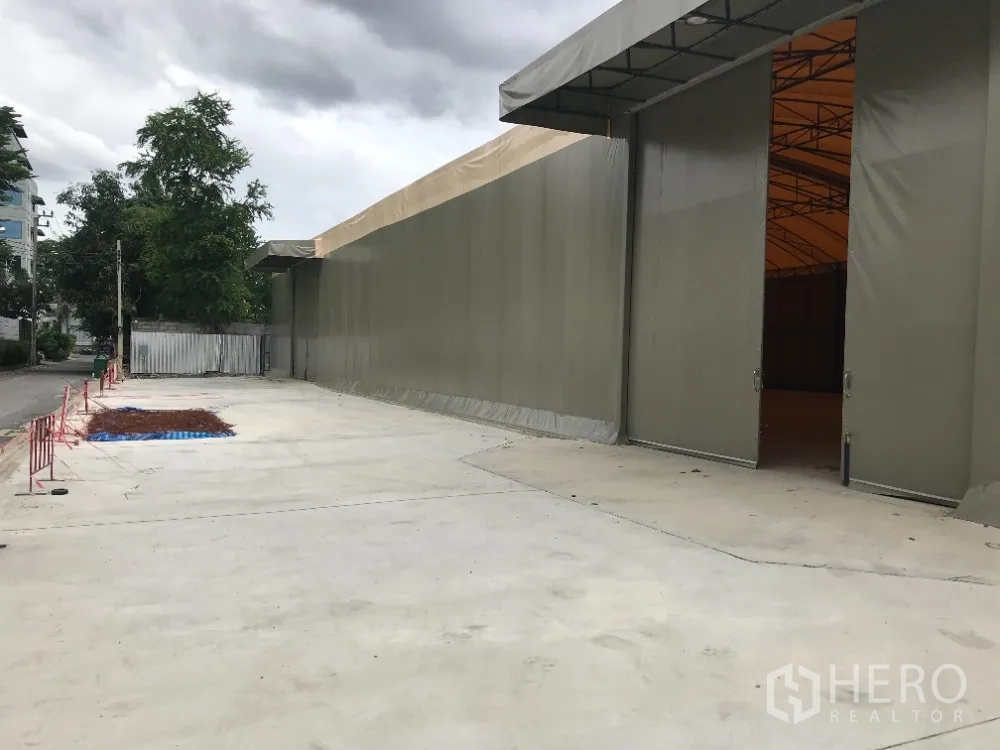 Warehouse for rent in Huai Khwang, Bangkok - Large sliding doors open to the warehouse, with a broad paved yard for truck access.
