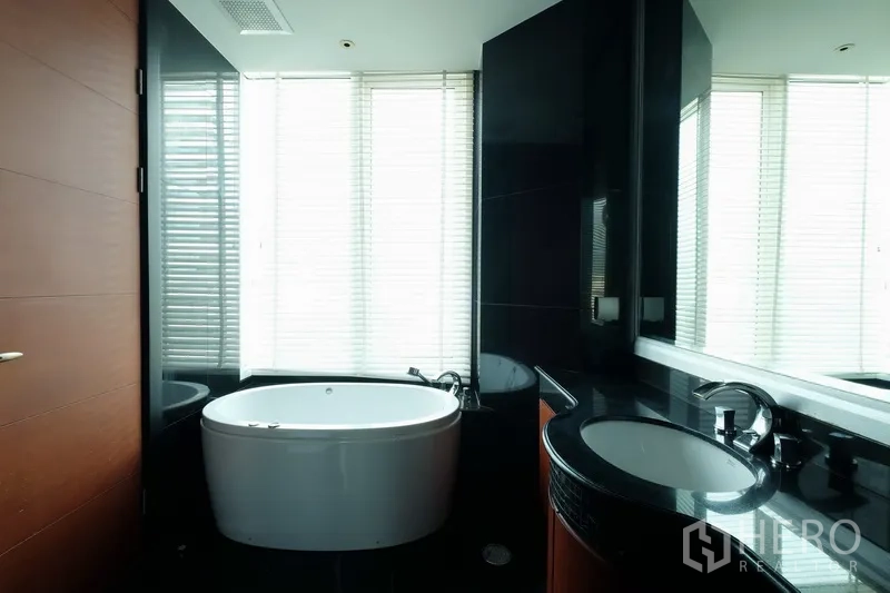 Condominium for rent in Bang Rak, Bangkok - Contemporary bathroom featuring a soaking bathtub, large mirror and curved vanity.
