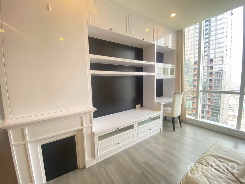 公寓 出租在Bang Rak, Bangkok - 白色定制置物与电视墙特写，窗边设有学习工作区。