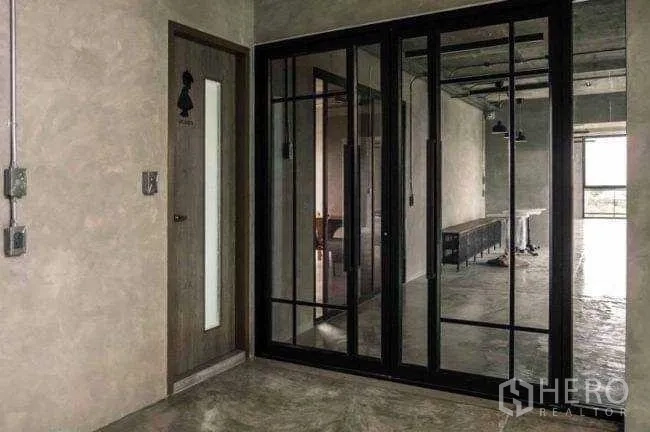 Office Space for rent or sale in Lak Si, Bangkok - Lobby corner with black-framed glass sliding partitions and exposed-concrete walls.