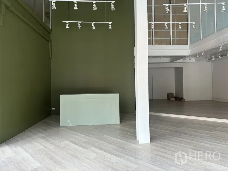 零售空间 出租在Khlong Toei, Bangkok - 绿墙与白色立柱，旁有玻璃夹层的展厅空间。