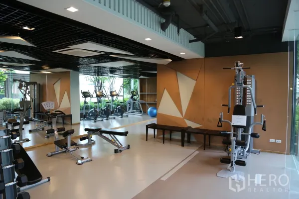 Condominium for rent in Huai Khwang, Bangkok - Modern fitness center with weight benches, multi-gym, treadmills and bikes, large mirrors and floor-to-ceiling windows.