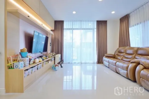 独立式住宅 出租或出售在Bang Kapi, Bangkok - 明亮客厅，通高落地窗、亮面地坪、真皮沙发与带储物的电视背景墙。