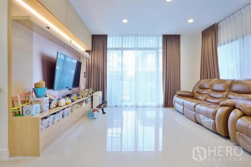 独立式住宅 出租或出售在Bang Kapi, Bangkok - 明亮客厅，通高落地窗、亮面地坪、真皮沙发与带储物的电视背景墙。