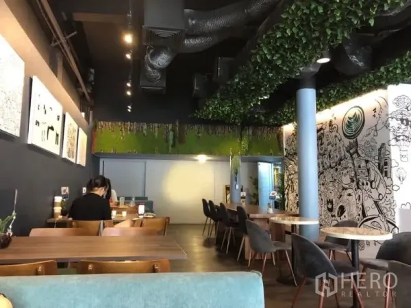店屋 出租在Ratchathewi, Bangkok - 现代餐厅式店屋内景，木质餐桌与软椅、绿植吊顶、外露风管、涂鸦特色墙与暖色灯光，临近地铁。