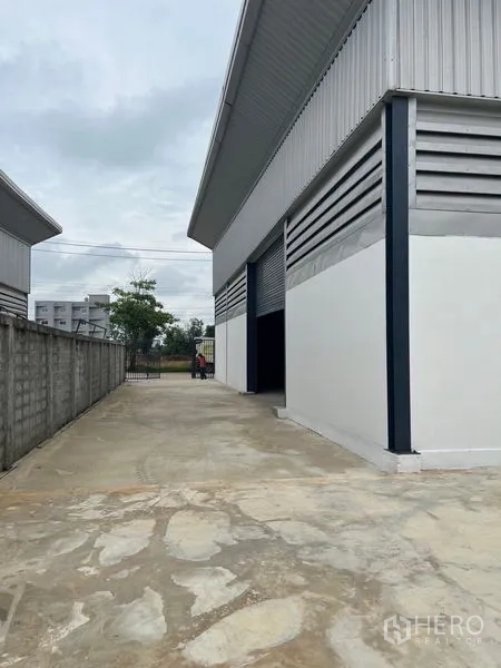 Warehouse for rent or sale in Sai Noi, Nonthaburi - Side driveway next to warehouse leading to front gate along boundary wall.