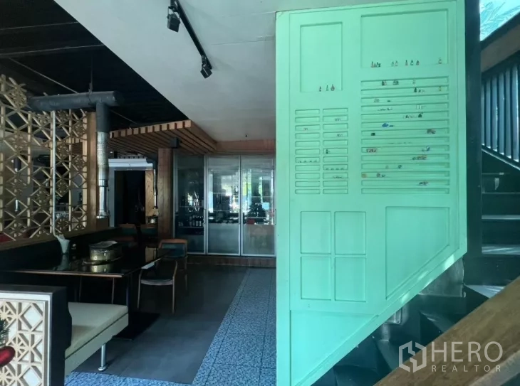 零售空间 出租在Watthana, Bangkok - 一层室内展示通往二层的楼梯、花纹地砖、座位与装饰隔断。