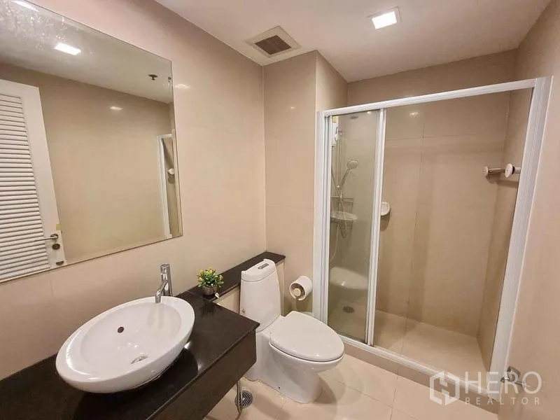 Condominium for rent in Khlong Luang, Pathum Thani - Modern bathroom with glass shower enclosure, vanity and toilet in neutral tones.