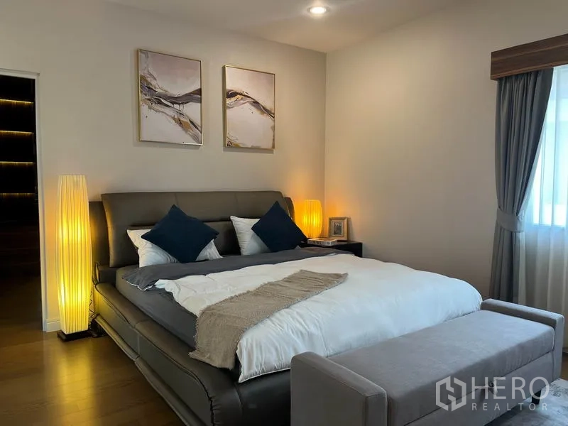Detached House for rent or sale in Prawet, Bangkok - Master bedroom with upholstered bed, bedside lamps and window drapes.