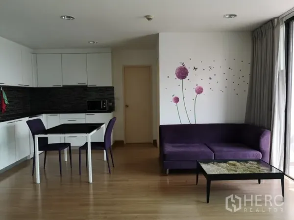 คอนโด ขายในWatthana, Bangkok - ครัวแบบเปิดตู้สีขาว ชุดโต๊ะทานอาหาร และโซฟาสีม่วงข้างหน้าต่างบานใหญ่