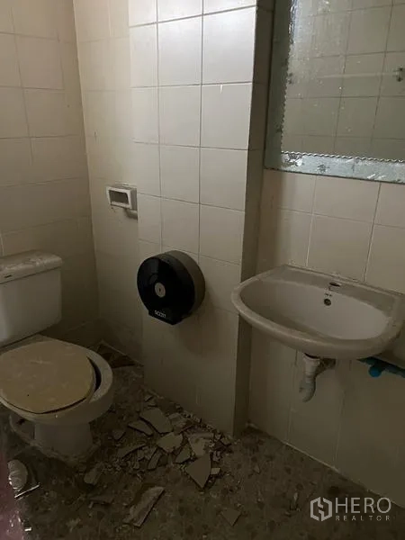Shophouse for rent in Watthana, Bangkok - Compact restroom with white tiles, toilet, sink and mirror awaiting renovation.