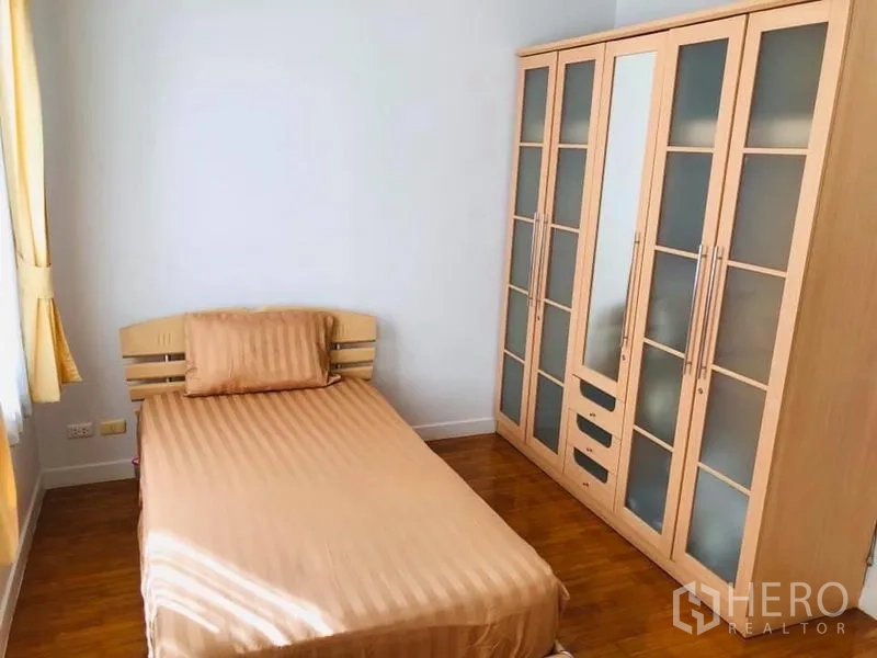 Townhouse for rent in Khlong Toei, Bangkok - Cozy bedroom with single bed, large glass-front wardrobe and wood floors.