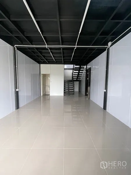 货栈 出租在Lam Luk Ka, Pathum Thani - 一层办公/展示区，亮面地砖，高黑色天花，后方设楼梯。