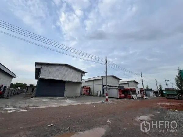 Warehouse for rent in Bang Khun Thian, Bangkok - Row of modern warehouses along an access road with power lines and site facilities.