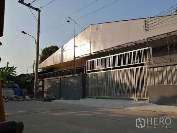 Warehouse for rent in Nonthaburi - Street view of the warehouse exterior with tall metal sliding gate and perimeter fence.