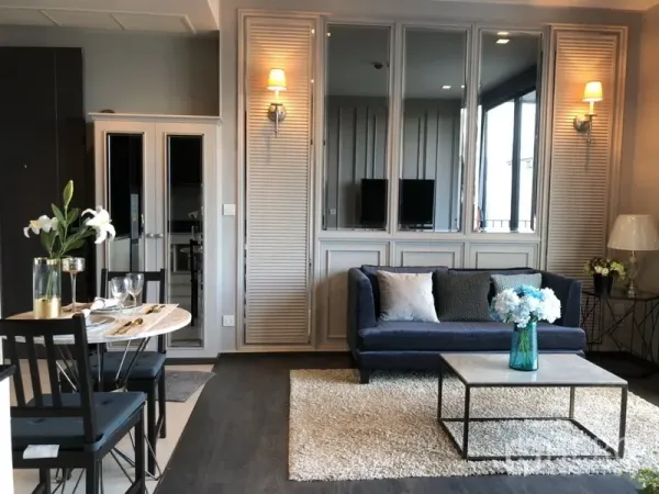 คอนโด ให้เช่าในWatthana, Bangkok - มุมนั่งเล่นอบอุ่น โซฟาสีน้ำเงิน โคมไฟติดผนัง ผนังกระจกเงา และโต๊ะกลาง ข้างมุมทานอาหาร