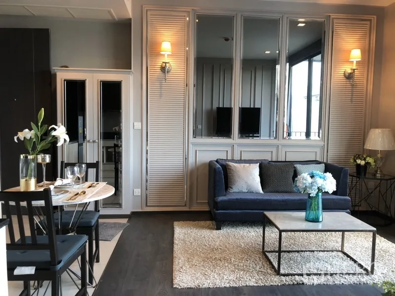 คอนโด ให้เช่าในWatthana, Bangkok - มุมนั่งเล่นอบอุ่น โซฟาสีน้ำเงิน โคมไฟติดผนัง ผนังกระจกเงา และโต๊ะกลาง ข้างมุมทานอาหาร