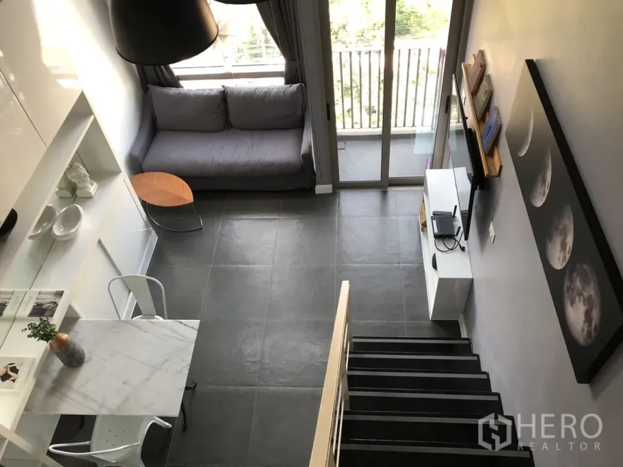 คอนโด ให้เช่าหรือขายในKhlong Toei, Bangkok - ห้องนั่งเล่นเพดานสูง โซฟาสีเทา ประตูระเบียง ตู้ทีวี โต๊ะอาหารท็อปหินอ่อน และบันได บนพื้นกระเบื้องสีเข้ม