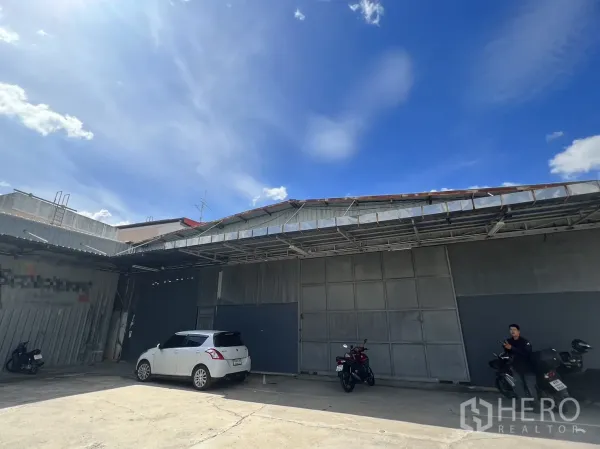 Warehouse for rent in Suan Luang, Bangkok - Front view of the warehouse showing wide roller shutter doors and paved forecourt parking.