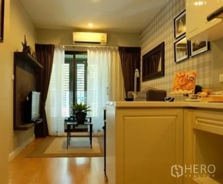 公寓 出租在Khlong Toei, Bangkok - 明亮客厅，开放式小厨房与电视墙，落地推拉门通往阳台。