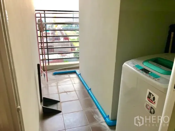 Condominium for rent in Huai Khwang, Bangkok - Utility balcony with washing machine, tiled floor, and metal railing overlooking the city.