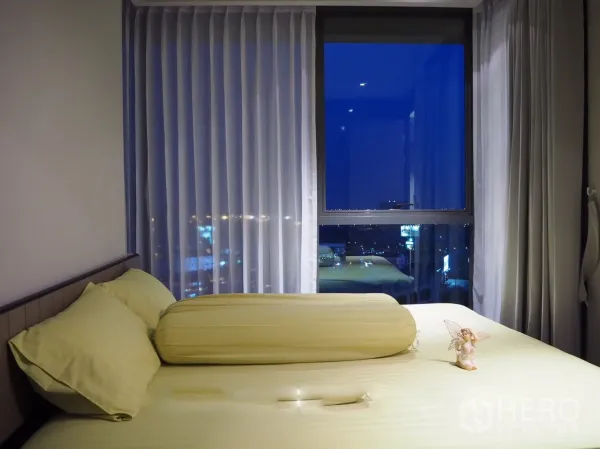 Condominium for rent in Khlong Toei, Bangkok - Cozy bedroom with large window, sheer curtains and night city view.