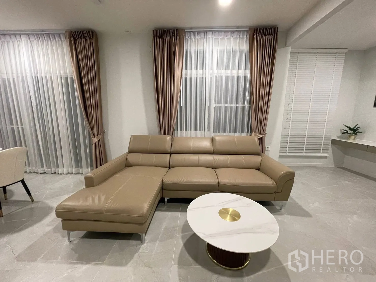 Detached House for rent in Prawet, Bangkok - Leather sectional sofa facing a round marble coffee table by tall windows.