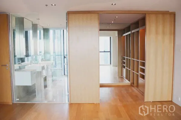 Condominium for rent or sale in Sathon, Bangkok - Master suite with walk-in closet and glass-enclosed bathroom with double vanity, set on hardwood floors.
