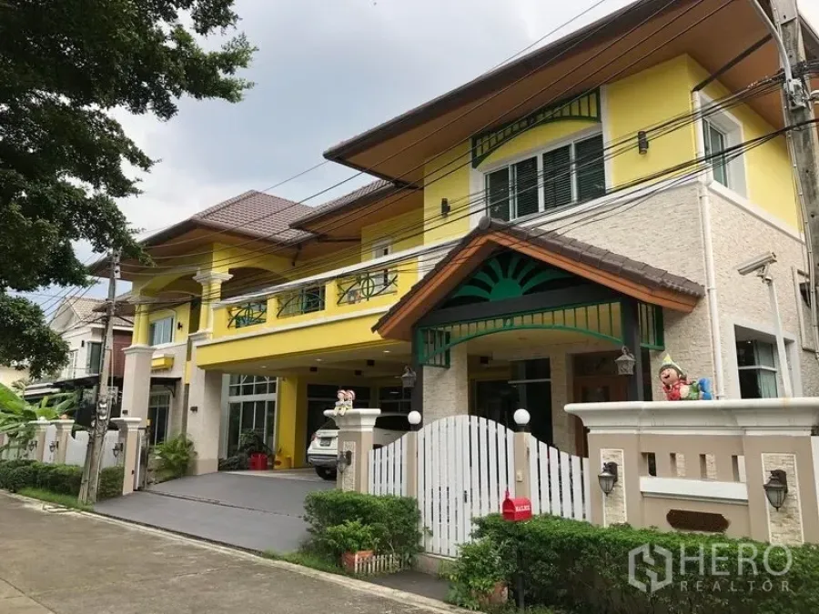 บ้าน ขายในWang Thonglang, Bangkok - บ้านเดี่ยวสองชั้นสีเหลืองพร้อมรั้วและโรงจอดรถในหมู่บ้านปลอดภัย