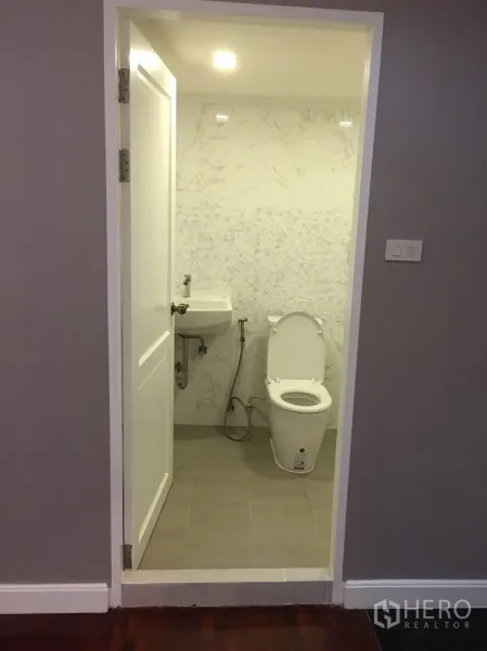 Condominium for rent in Watthana, Bangkok - Modern bathroom with marble-look wall tiles, compact basin, bidet spray and floor-mounted toilet.