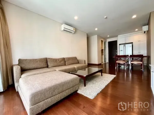 Condominium for rent in Watthana, Bangkok - Living area with sectional sofa, glass coffee table, and dining space in the background.