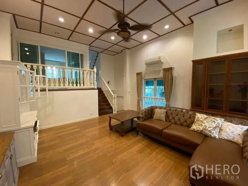 联排别墅 出租或出售在Mueang Samut Prakan, Samut Prakan - 起居区配L形皮沙发、楼梯与展示柜。