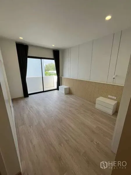 Townhouse for rent or sale in Don Mueang, Bangkok - Bright room with wood flooring, wall paneling and a sliding glass door opening to the balcony.