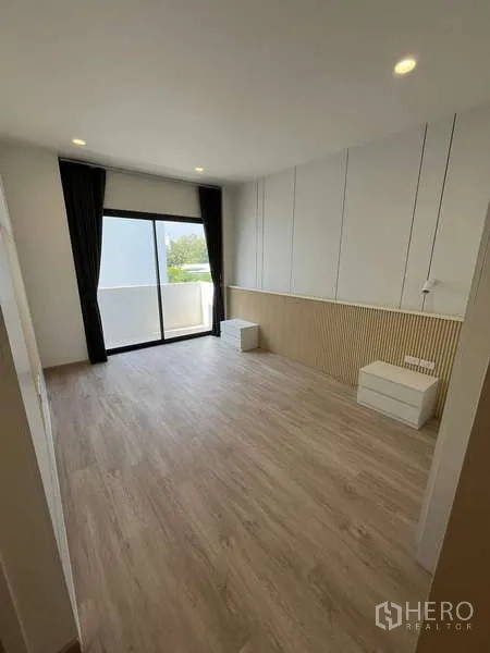 Townhouse for rent or sale in Don Mueang, Bangkok - Bright room with wood flooring, wall paneling and a sliding glass door opening to the balcony.