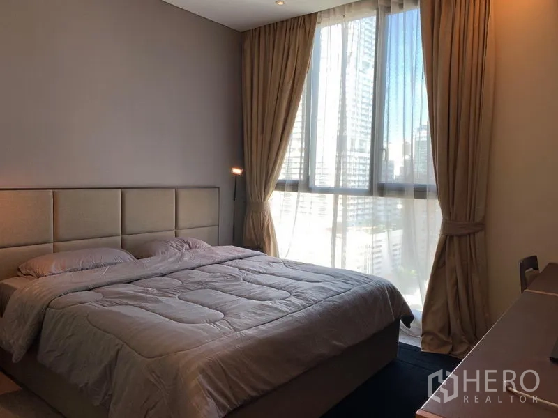 Condominium for rent in Watthana, Bangkok - Cozy master bedroom with large window, blackout curtains and a city outlook in neutral tones.
