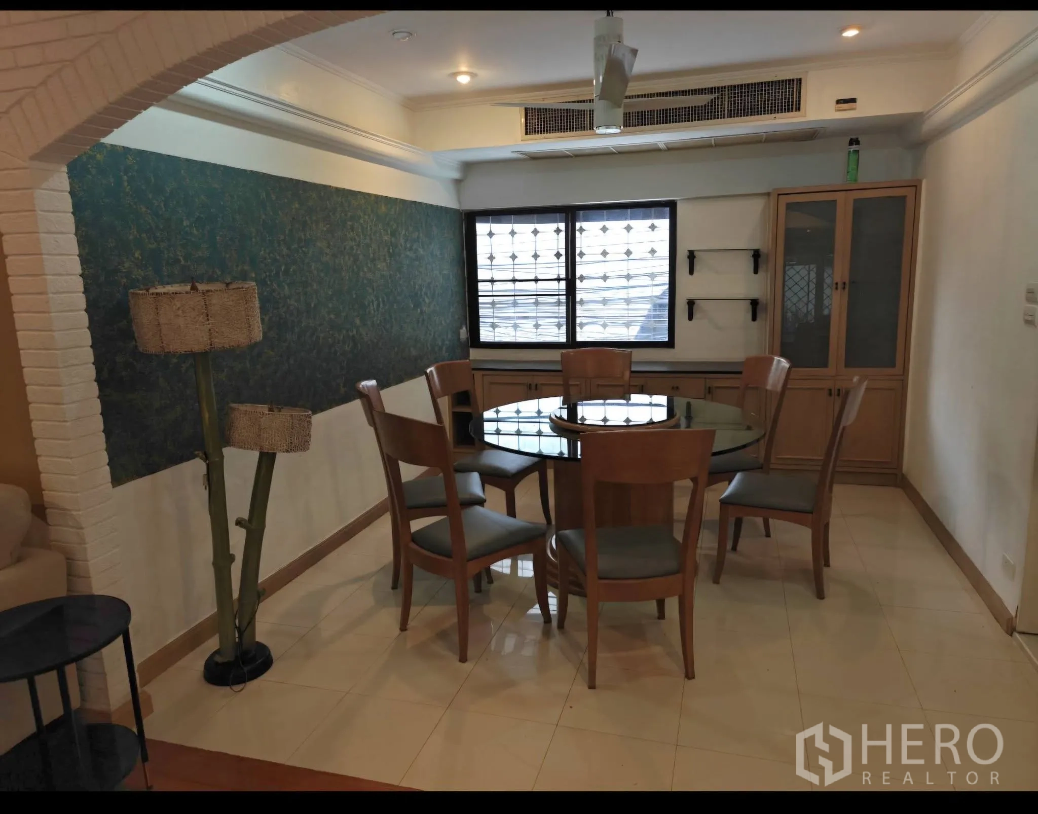 Condominium for rent in Sathon, Bangkok - Dining area with round glass table and six chairs, built-in cabinet, and feature wall under an arch.