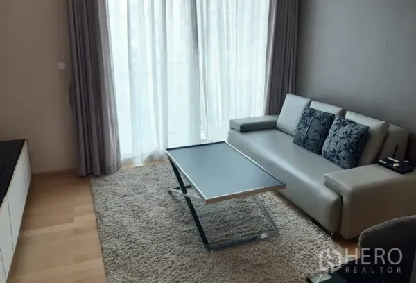 คอนโด ให้เช่าในKhlong Toei, Bangkok - ห้องนั่งเล่นโปร่งสบาย โซฟาสีเทา โต๊ะกลางทรงบาง พรม และผ้าม่านโปร่งเต็มผนัง