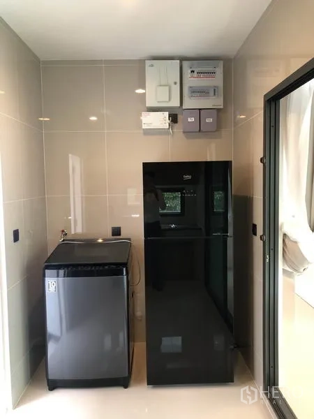 Detached House for rent or sale in Bang Kapi, Bangkok - Utility area with refrigerator, washing machine and control panels beside a sliding door.